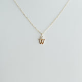 Gold necklace with a 'W' pendant on a light gray background
