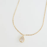 Gold necklace with a teardrop-shaped pendant on a light gray background