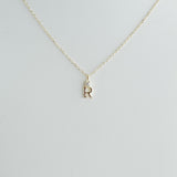 Gold necklace with a 'R' pendant on a light gray background