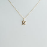 Gold necklace with a 'M' pendant on a light gray background