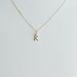 Gold necklace with a 'K' pendant on a light gray background