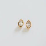 Pair of teardrop-shaped earrings with clear gemstones on a light gray background