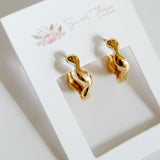 Gold snake-shaped earrings on a white card with floral design