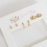 Set of gold earrings on a 'Sweet Three' branded card with floral design.
