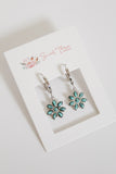 Floral earrings on a 'Sweet Three' branded card with a white background